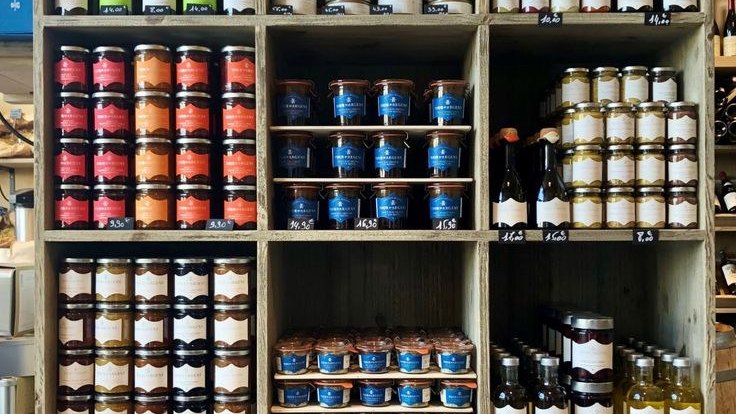 Étagères de l'épicerie fine : bocaux de confitures, terrines et bouteilles rangés par familles de produits.